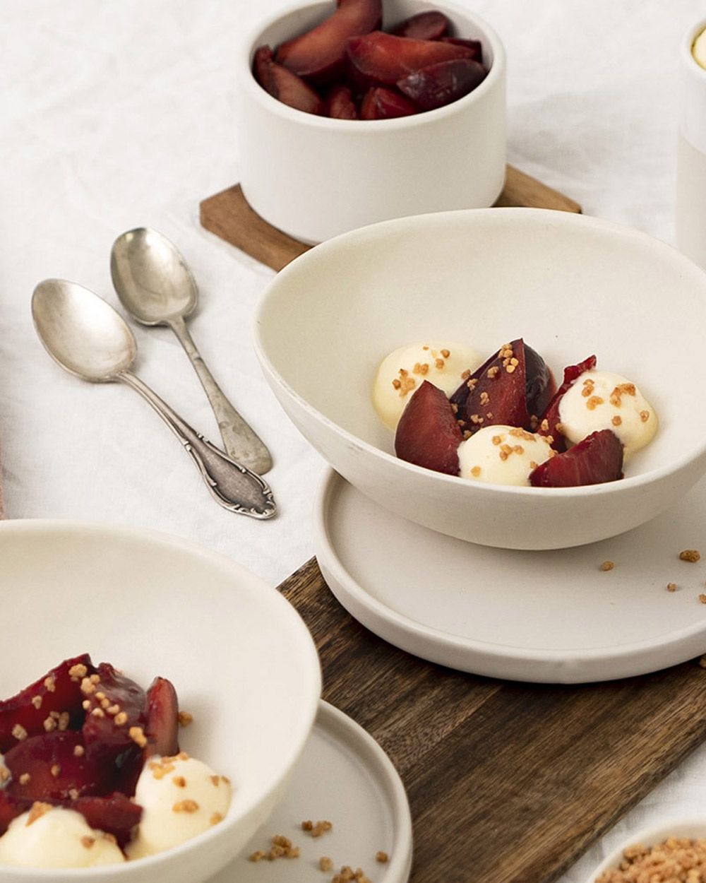 Zwei Schüsseln mit Pflaumen und weißem Schaum, daneben Besteck und eine weitere Schale mit Pflaumenstücken. 