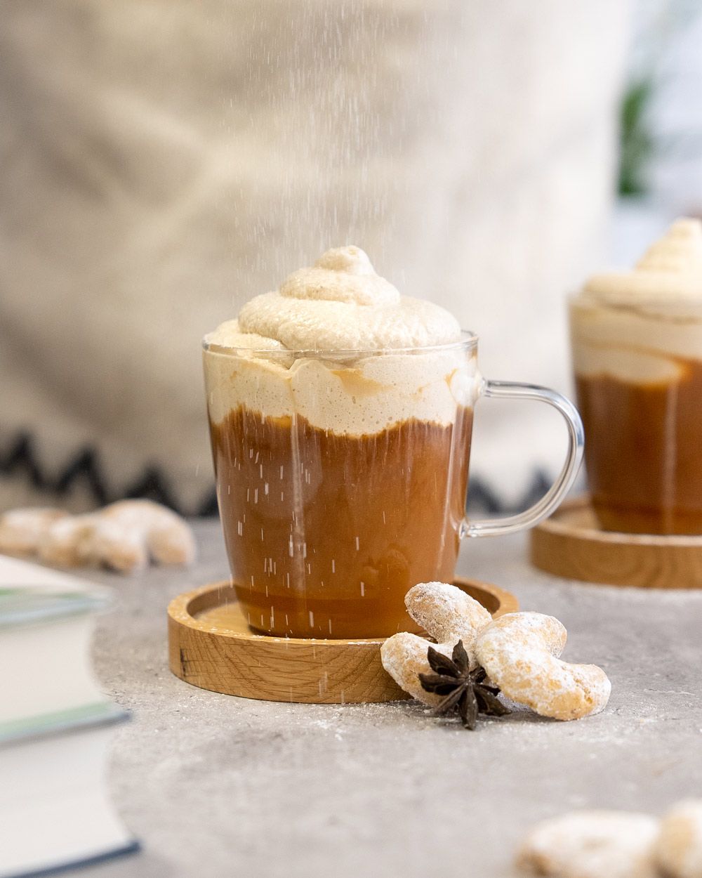 Ein Glas mit Kaffee mit Vanillekipfertopping, daneben ein weiteres Glas und Vanillekipferl.