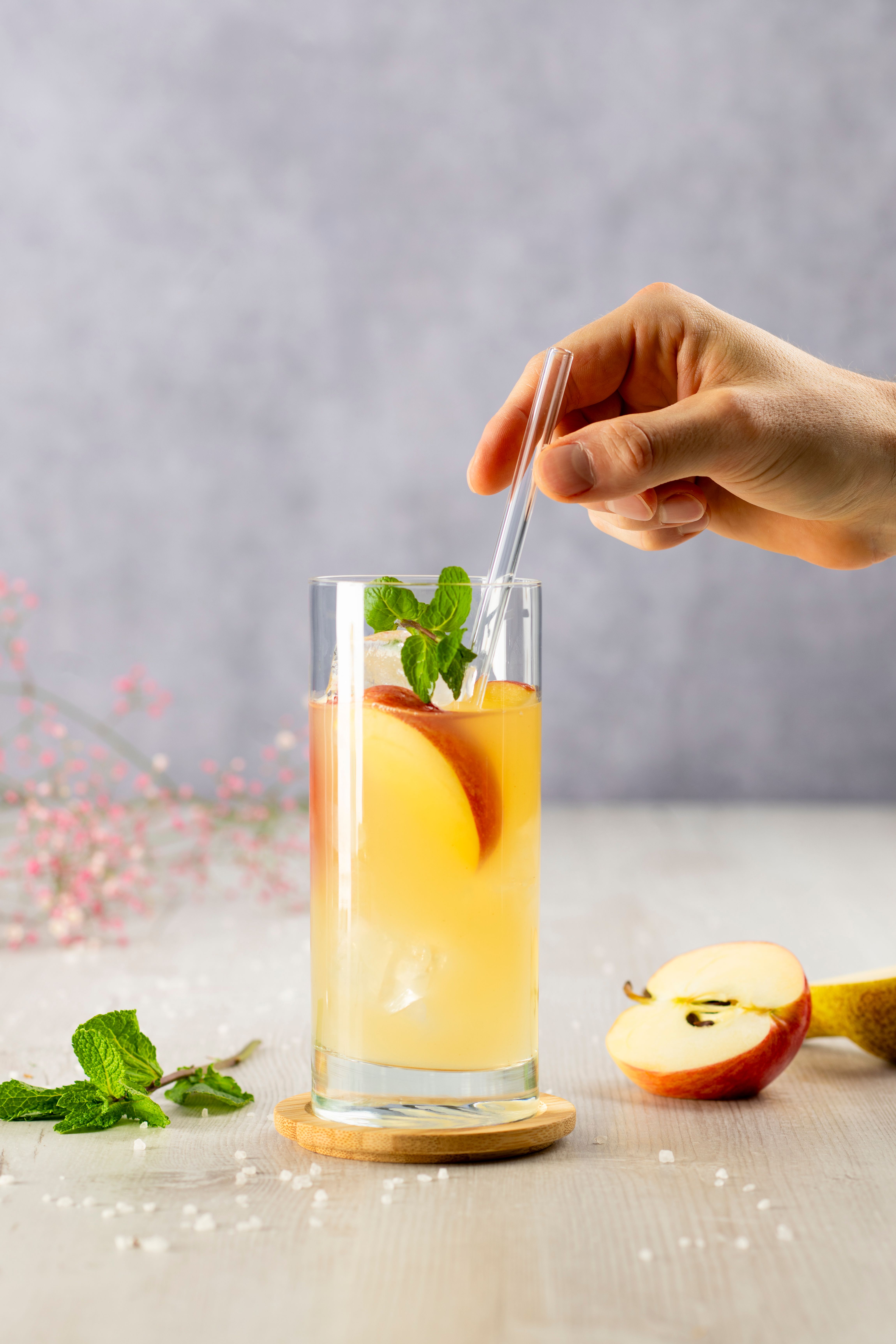 Jemand gibt einen Strohhalm in ein Glas mit Electro Fizz, daneben Äpfel. 