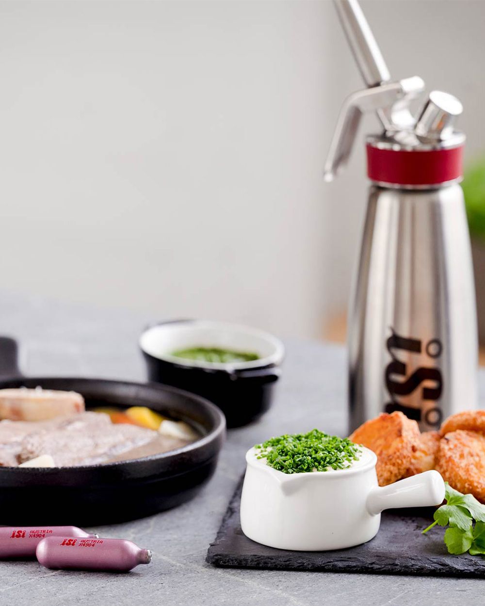 Mehrere Schüsseln mit Gerichten, eine davon Schnittlauchsauce. Daneben zwei iSi Charge Kapseln und ein iSi Sahnespender. 