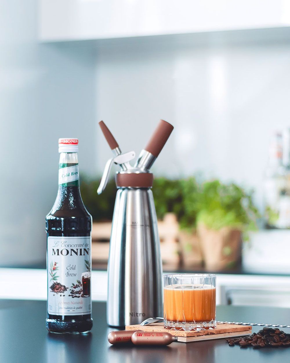 Ein Glas mit Nitro Whisky, daneben iSi Charge Kapseln, ein iSi Nitro und Monin Sirup.