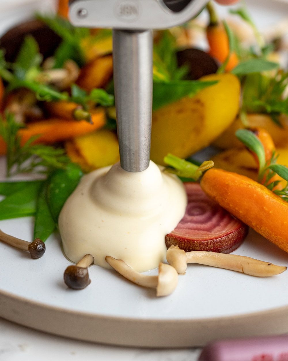 Jemand sprüht mit einem iSi Gourmet Whip Polentaschaum auf einen Teller mit Gemüse. 