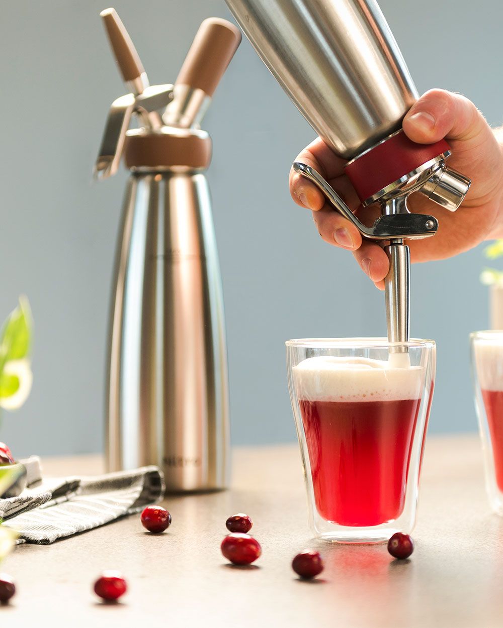 Jemand sprüht mit einem iSi Gourmet Whip Schaum auf einen Nitro Red Cheese Tea, daneben steht ein iSi Nitro. 