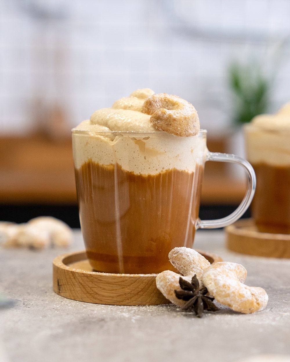 Ein Glas mit Kaffee mit Vanillekipfertopping, daneben ein weiteres Glas und Vanillekipferl.