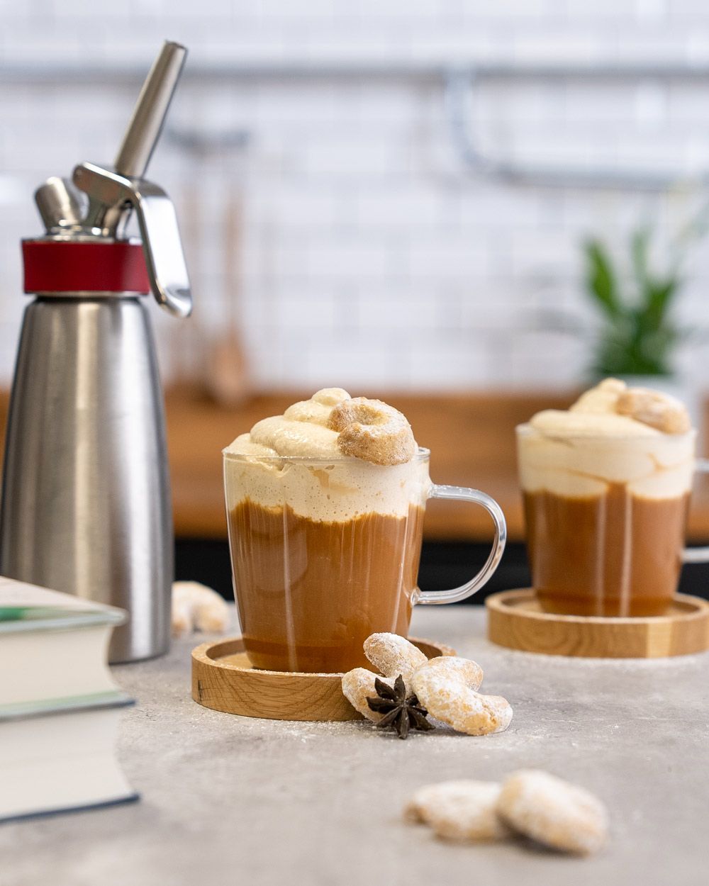 Zwei Gläser mit Kaffee mit Vanillekipferltopping, daneben  Vanillekipferl und ein iSi Gourmet Whip.