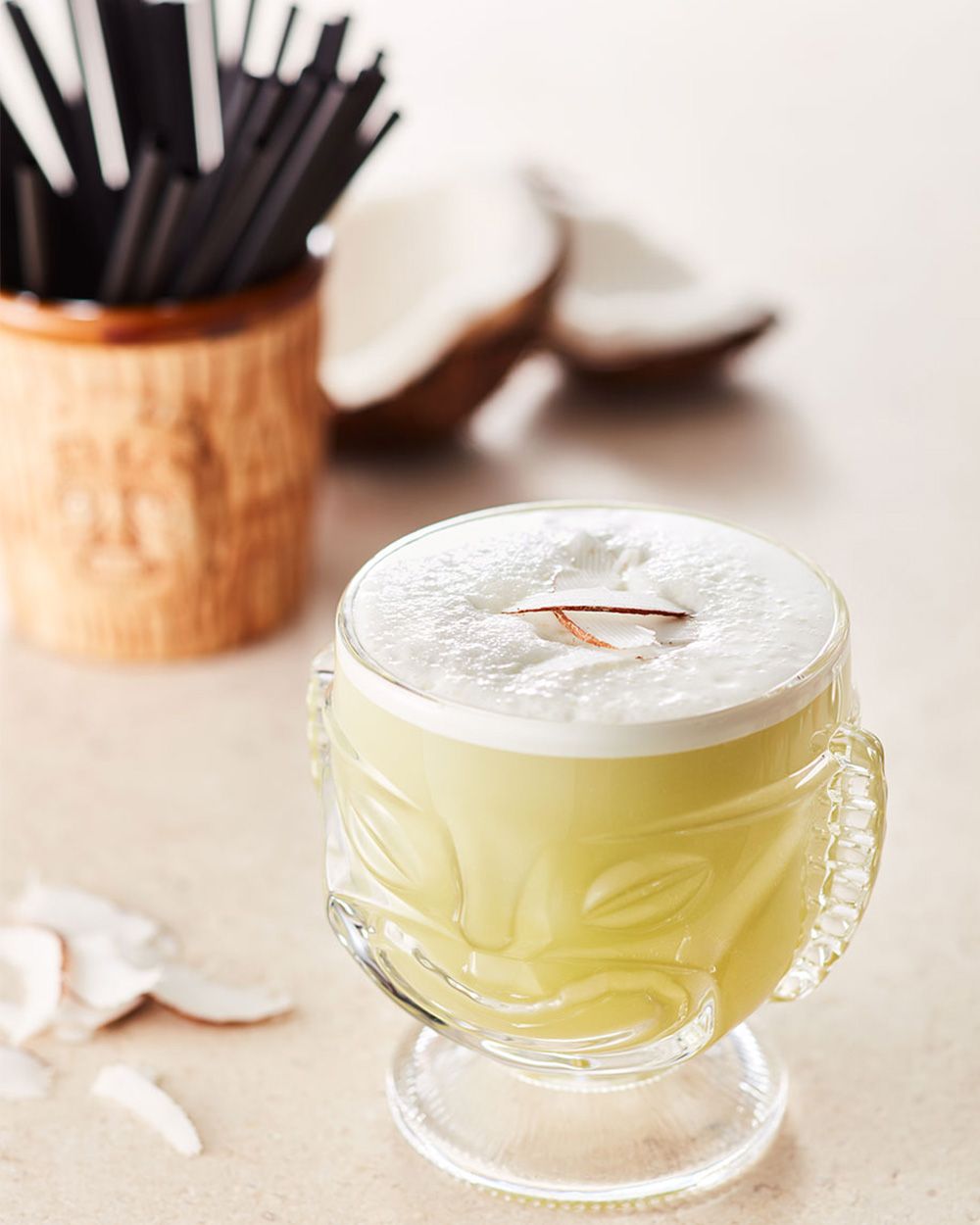 Ein Glas mit Nitro Kurkuma Tee, im Hintergrund Strohhalme und eine offene Kokosnuss. 