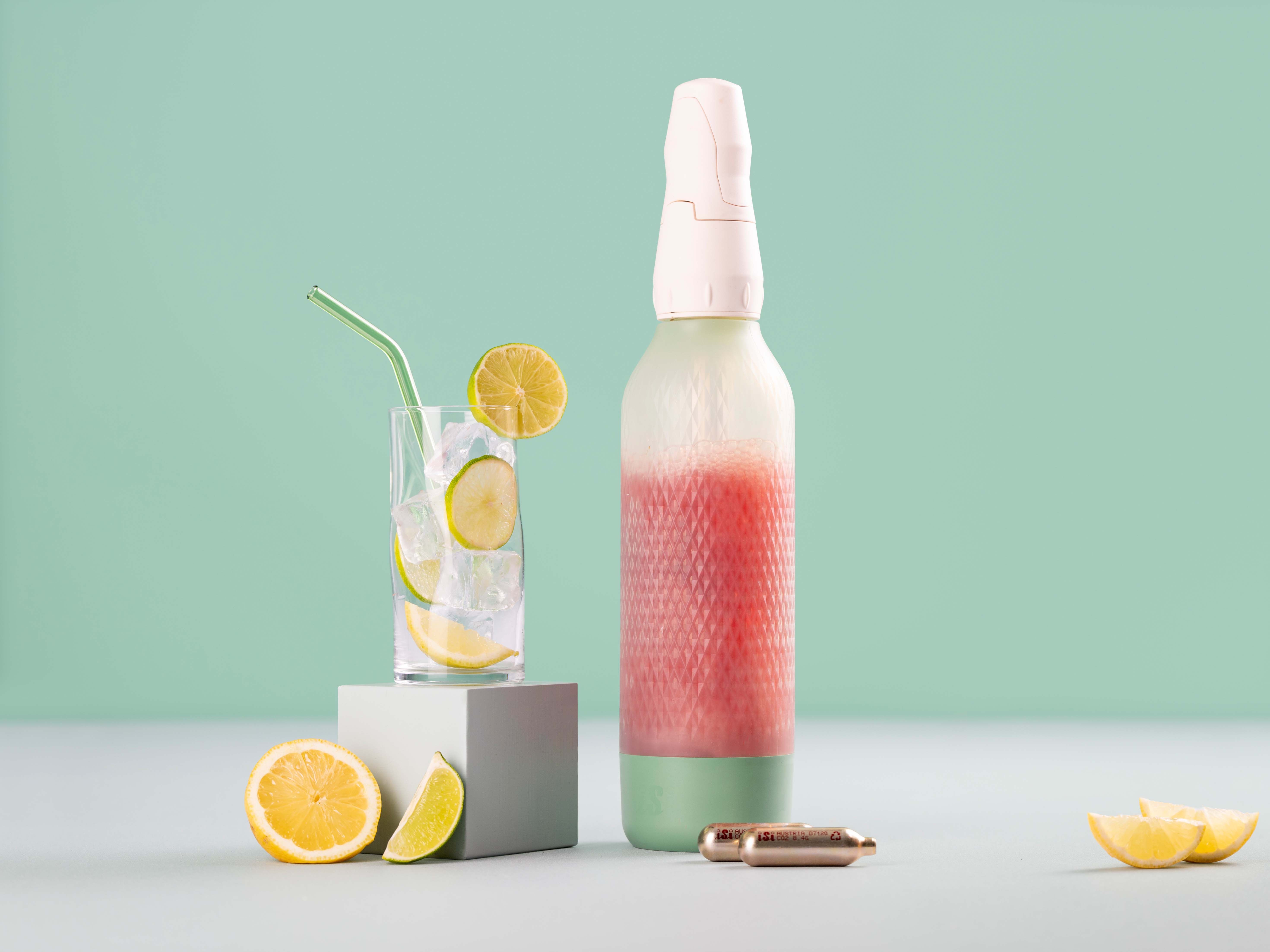 Ein Glas mit Eis und Zitronen, daneben ein iSi Twist'n Sparkle gefüllt mir Cranberry Ginger Lemonade und iSi Charge Kapseln. 