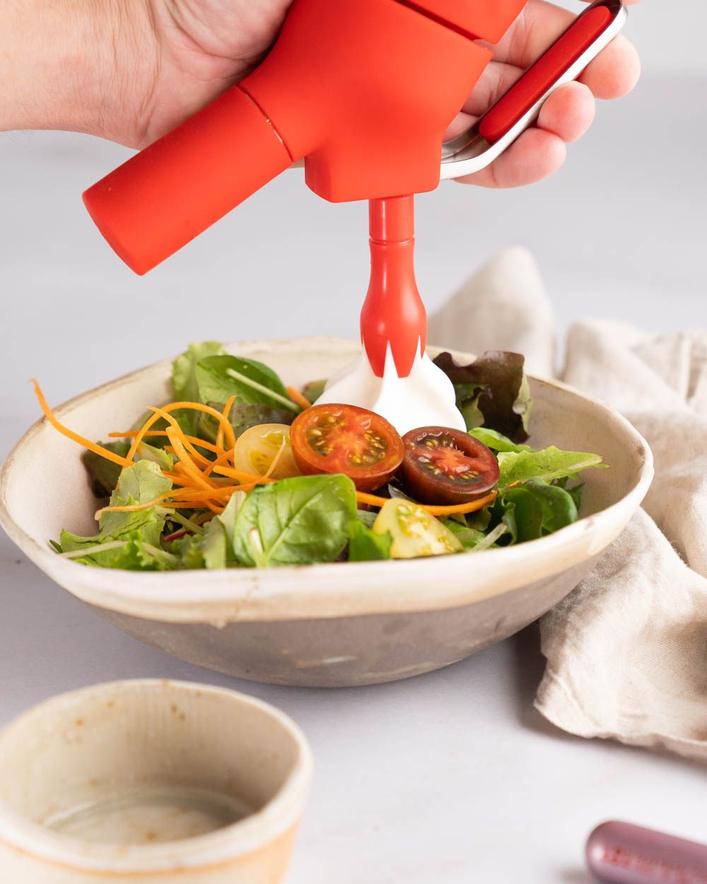 Jemand sprüht Sour Cream Dressing in eine Schüssel mit Salat.