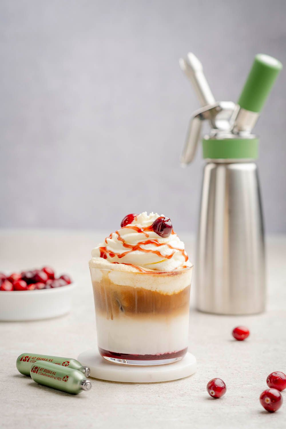 Ein Cherry Latte mit Mandelschaum, daneben liegen zwei grüne iSi-Sahnekapseln, im Hintergrund steht eine iSi Green Whip.