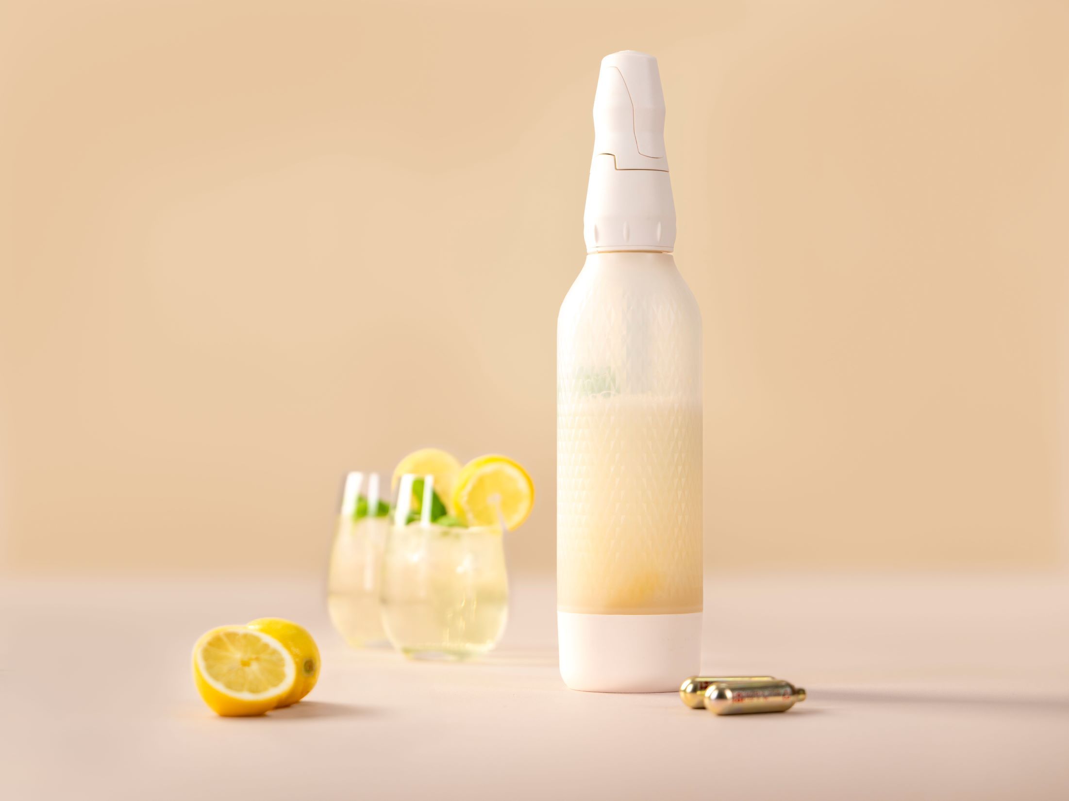 Ein weißer iSi Twist'n Sparkle gefüllt mit Fizzy Iced Tea, daneben zwei Gläser ebenfalls mit Iced Tea, iSi Charge Kapseln und Zitronen. 