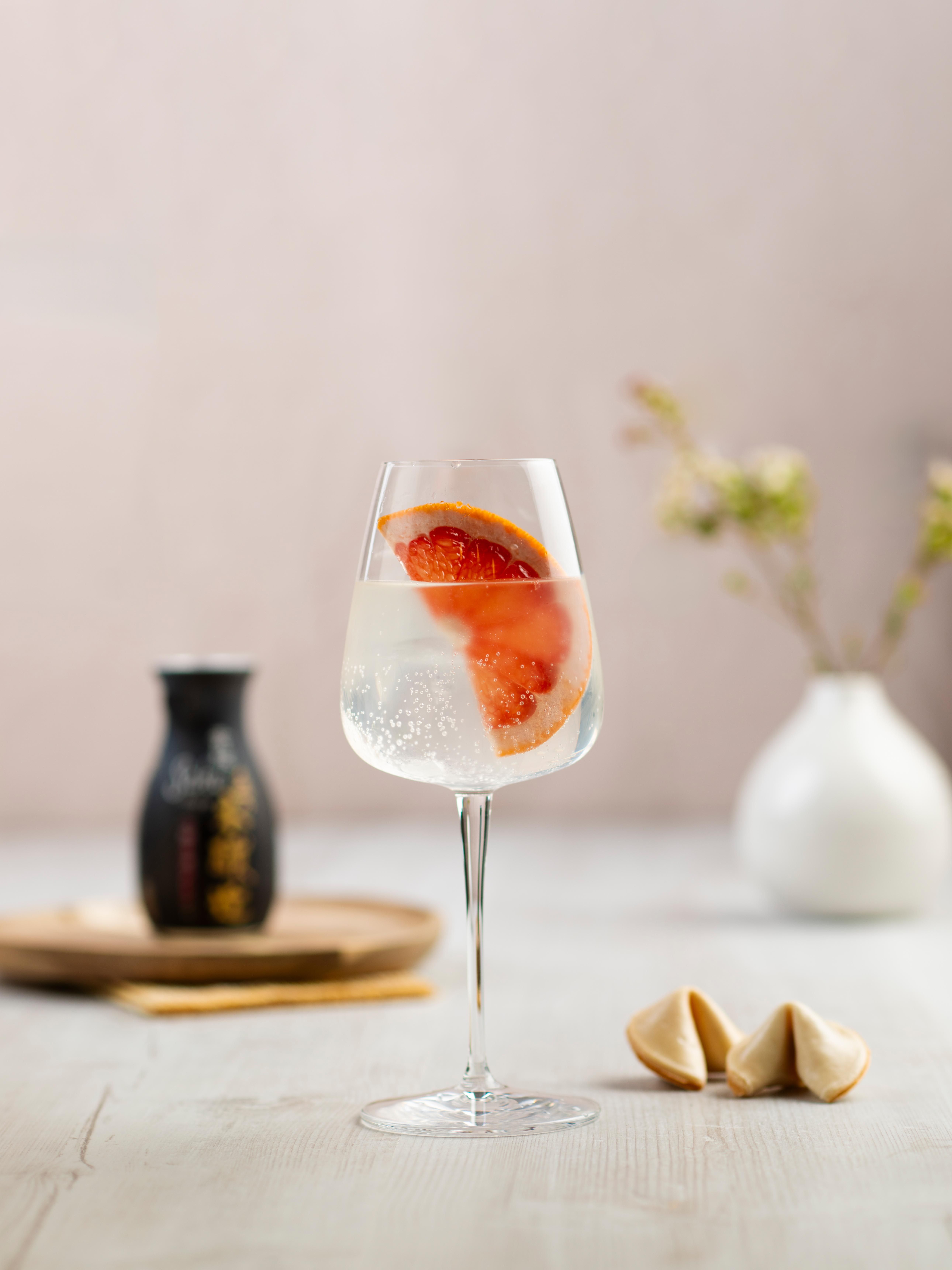 Ein Glas mit Sake Spritz und einer Scheibe Grapefruit, daneben Glückskekse und eine Karaffe Sake.