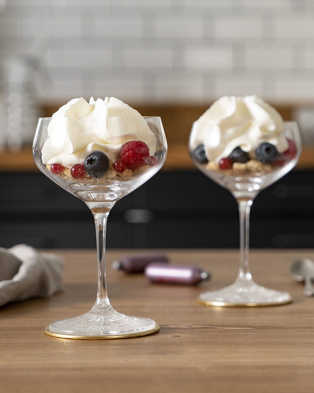 Zwei Gläser mit Beeren und Cheesecake Schaum. Im Hintergrund liegen zwei iSi Charger Kapseln. 