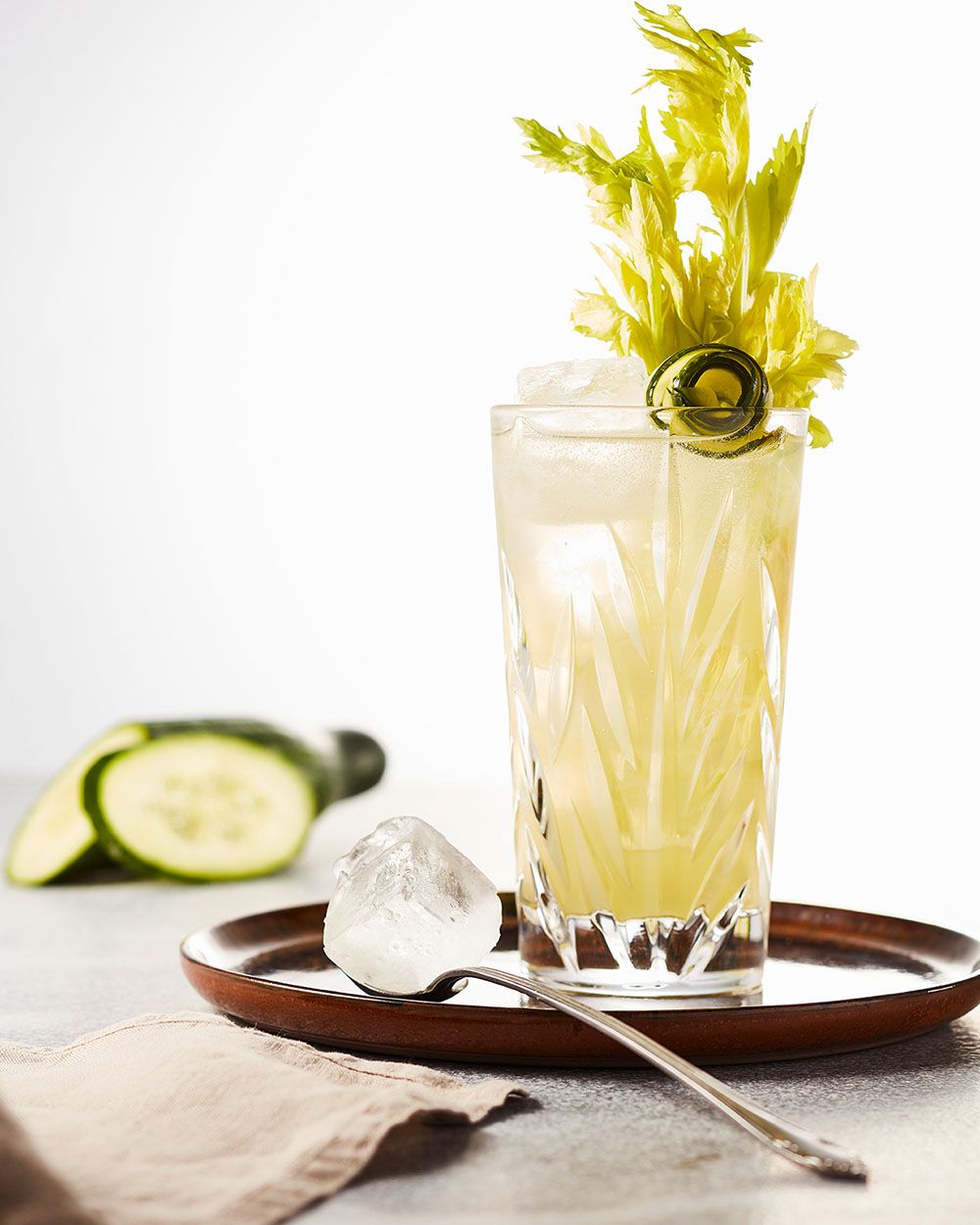 Ein schön dekoriertes Glas mit einem gelben Cocktail, im Hintergrund eine Gurke. 