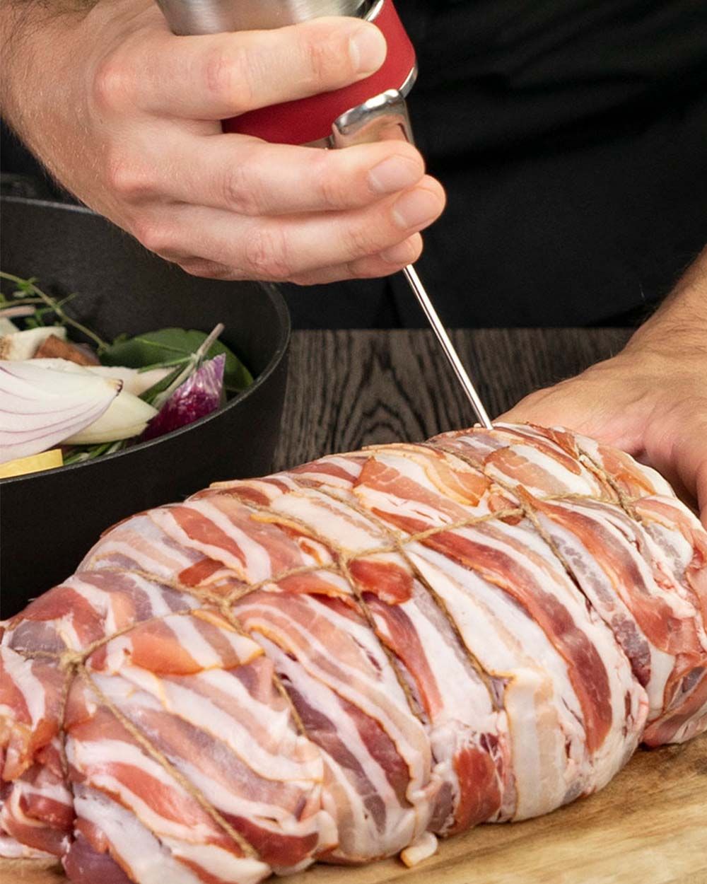 Jemand gießt mit einem iSi Gourmet Whip Sauce über ein mit Speck umwickeltes Stück Fleisch. 