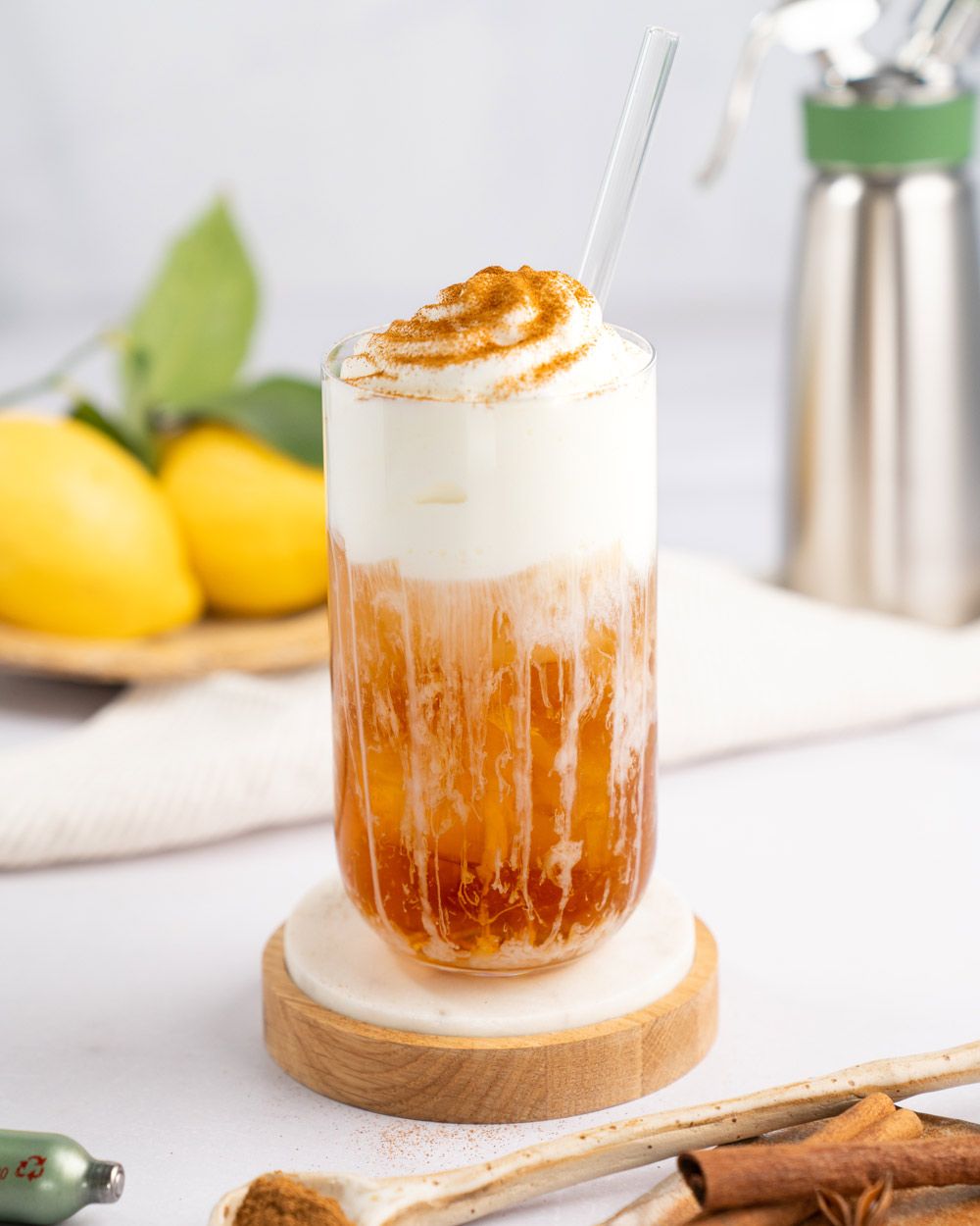 Ein Glas mit Eistee mit Sweet Cream Topping, im Hintergrund Zitronen und ein iSi Gourmet Whip. 