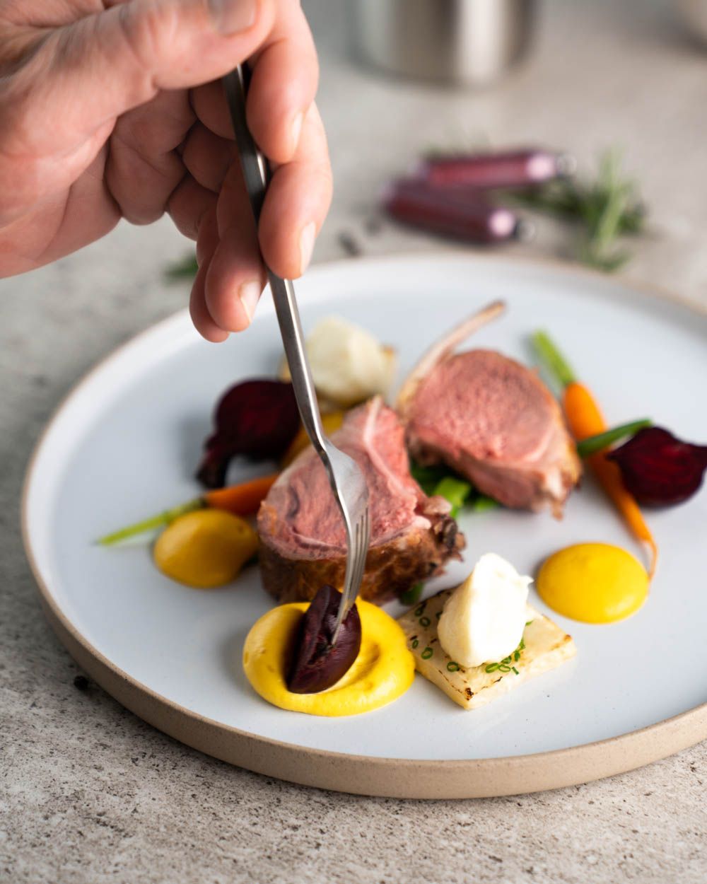 Jemand benutzt einen Löffel um einen Teller mit Lamm-Filets und Süßkartoffel Espuma zu dekorieren. 