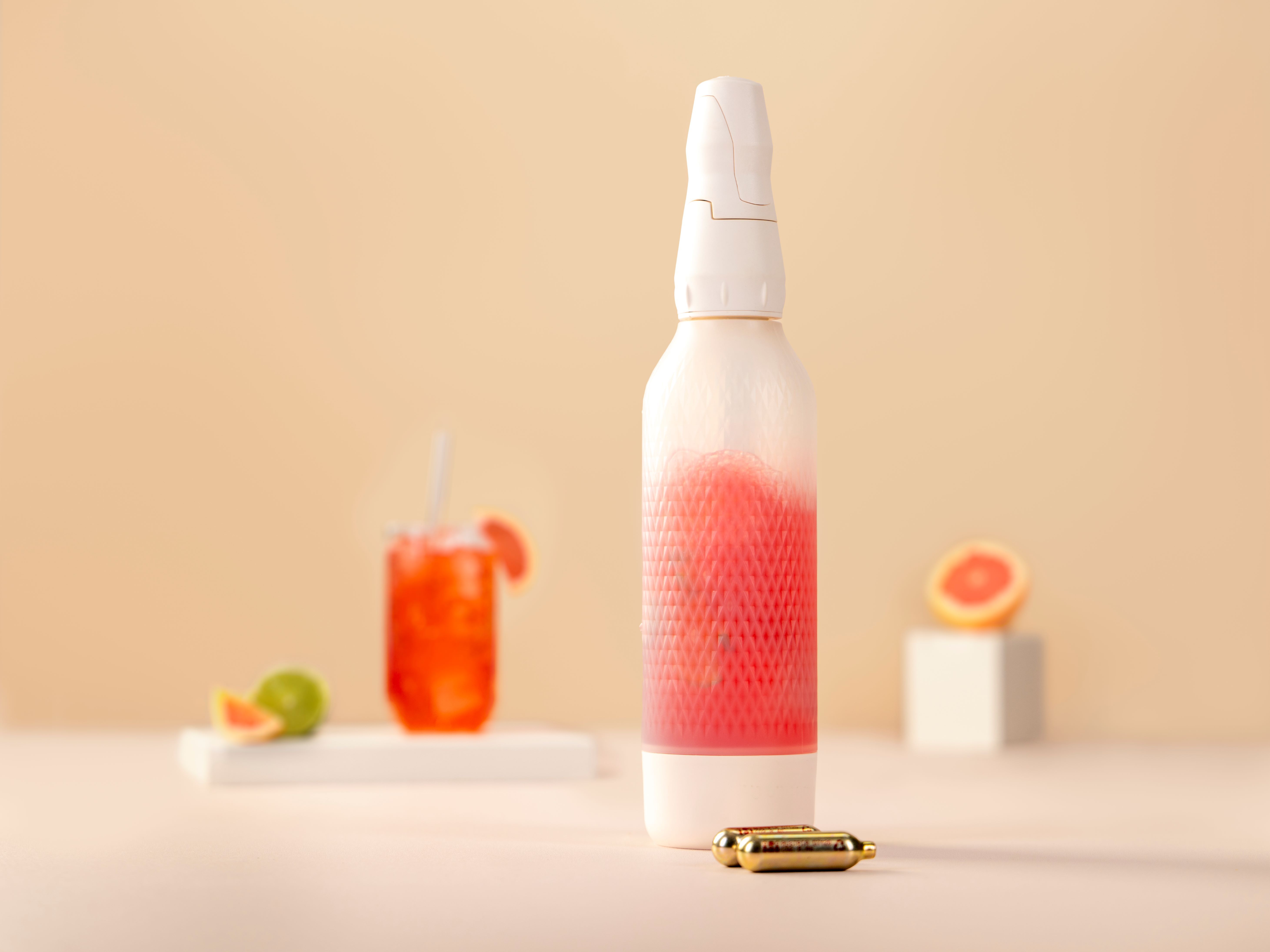 Ein iSi Twist'n Sparkle mit Paloma Twist, davor iSi Charge Kapseln, im Hintergrund eine Grapefruit und ein Glas mit Paloma Twist. 