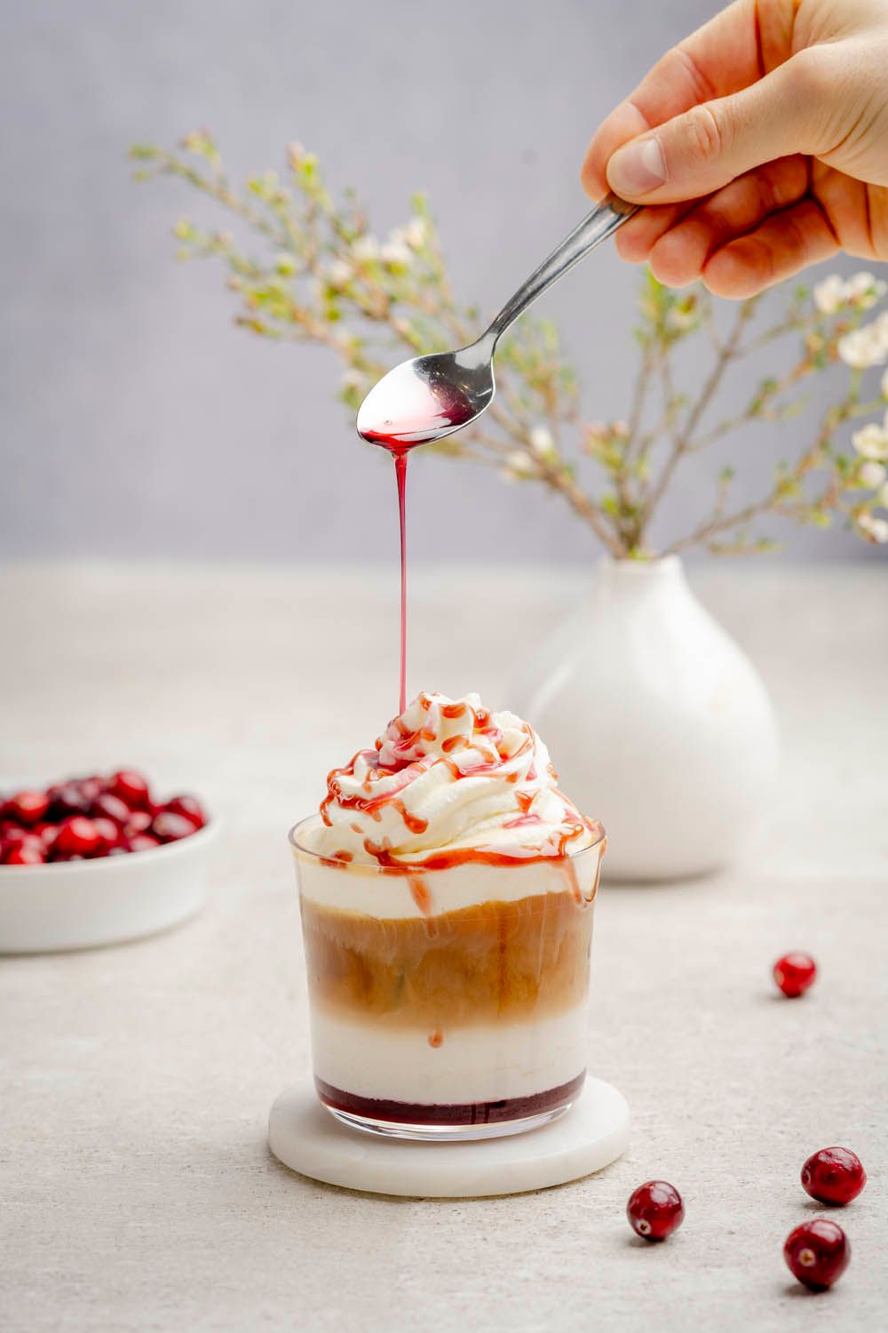 Jemand gießt mit einem Löffel Kirschsauce auf den Mandelschaum auf einem Cherry Latte. 