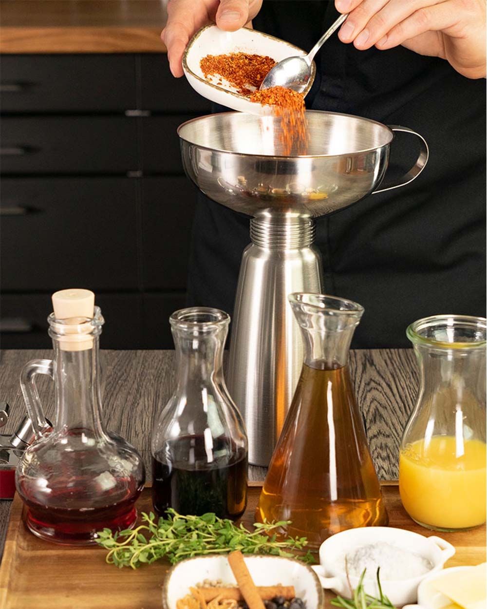 Jemand gibt Gewürze in ein iSi Gourmet Whip, davor stehen verschiedene Öle in Krügen.
