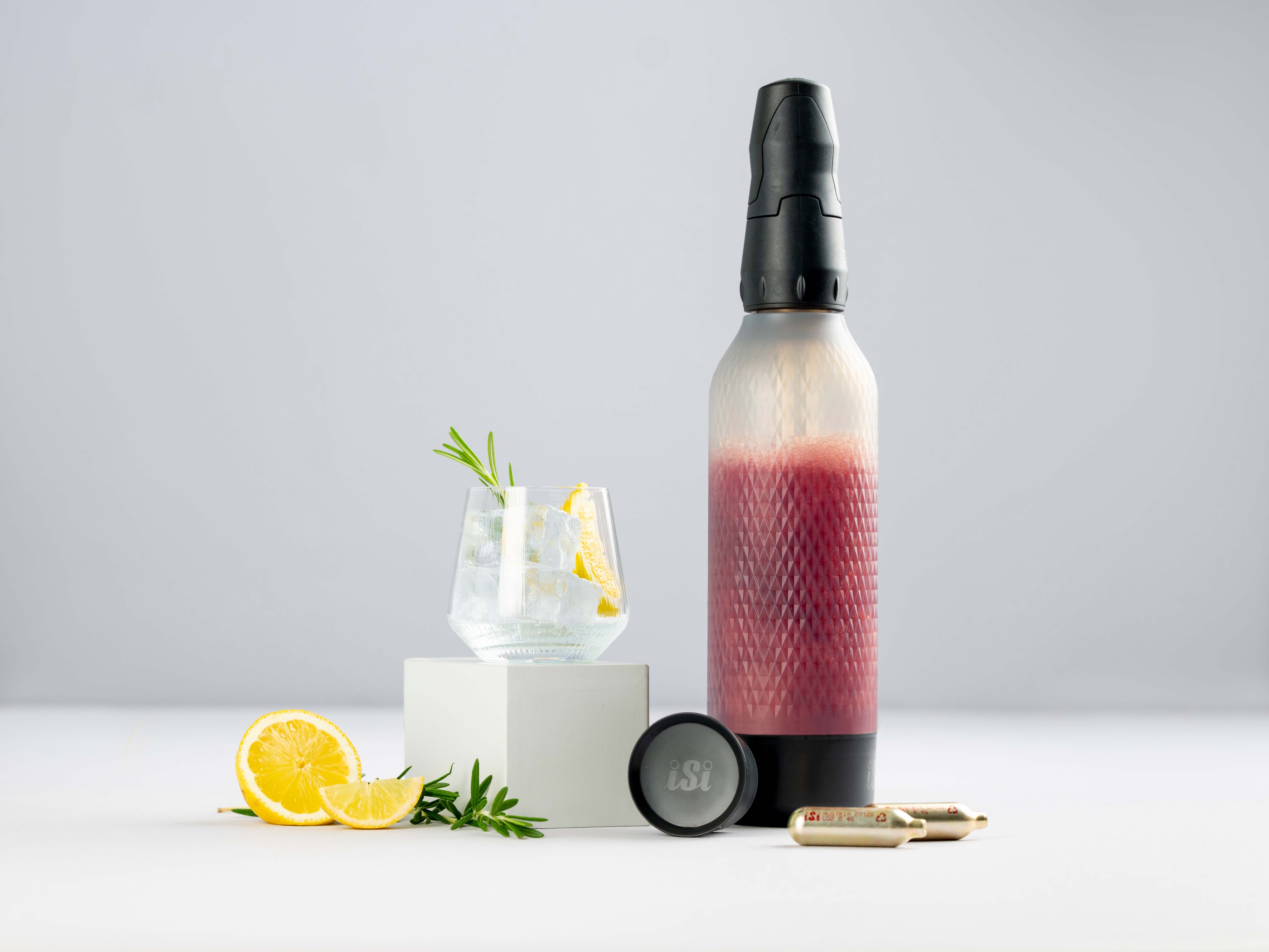 Ein Glas mit einem dunkelroten Getränk – Carbonized Black Currant – daneben Zitronen, iSi Charge Kapseln und ein iSi Twist'n Sparkle. 