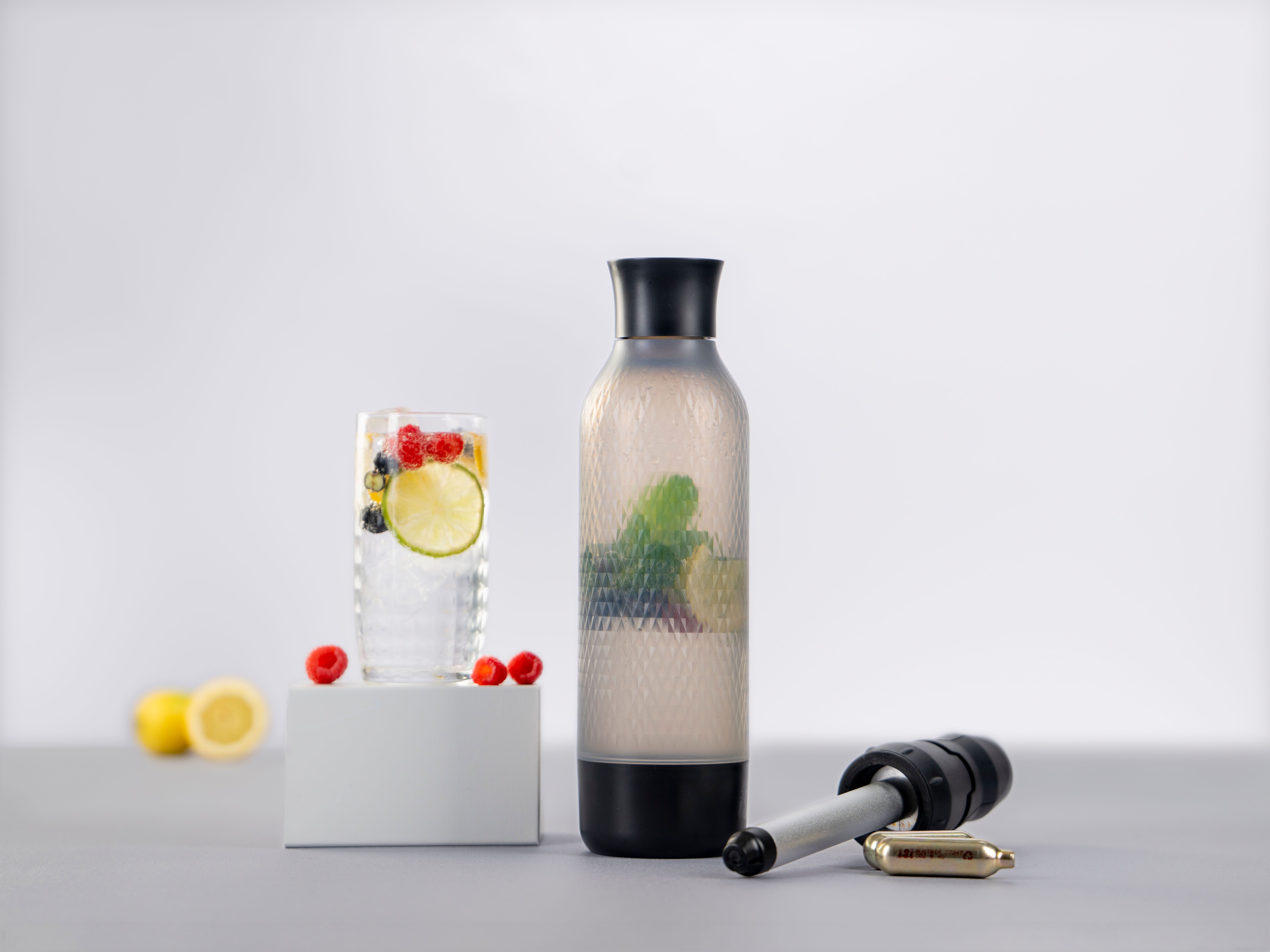 Ein Glas mit Sparkled Infused Wasser und Früchten, daneben weitere Früchte, ein iSi Twist'n Sparkle und iSi Charge Kapseln.