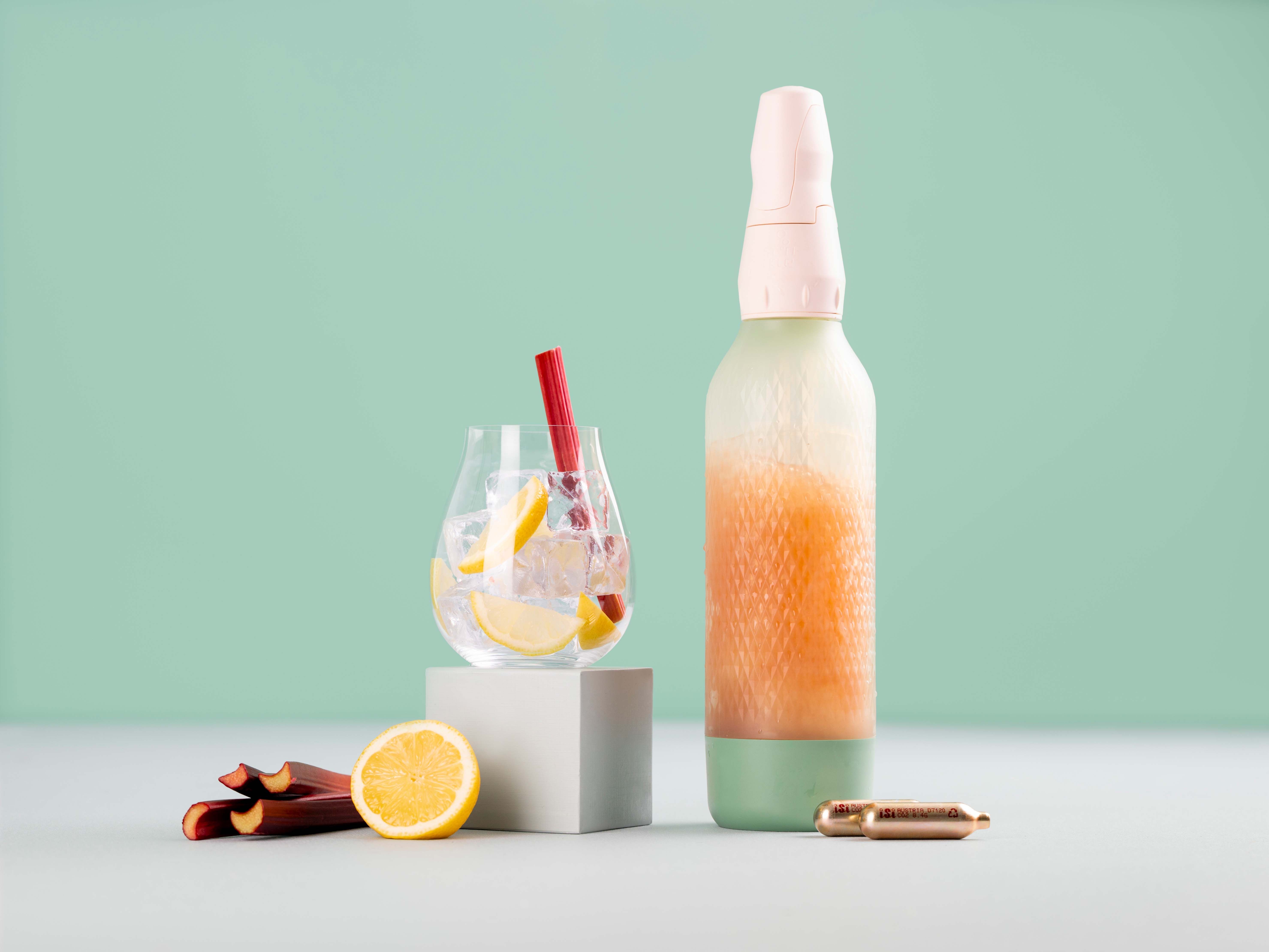 Ein Glas mit Eiswürfeln und Zitronen, daneben  Rhabarber, ein iSi Twist'n Sparkle und iSi Charge Kapseln.