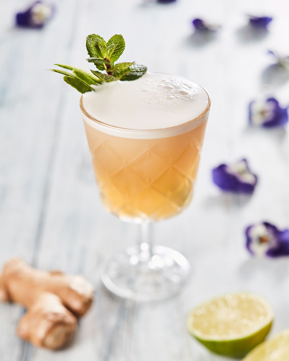 Ein Glas mit Nitro Mule, daneben Limetten, Ingwer und Veilchen. 