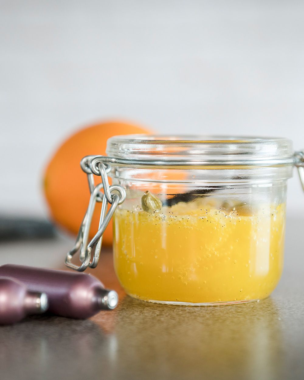 Ein Glas mit Orangensalat, daneben zwei iSi Charge Kapseln. 