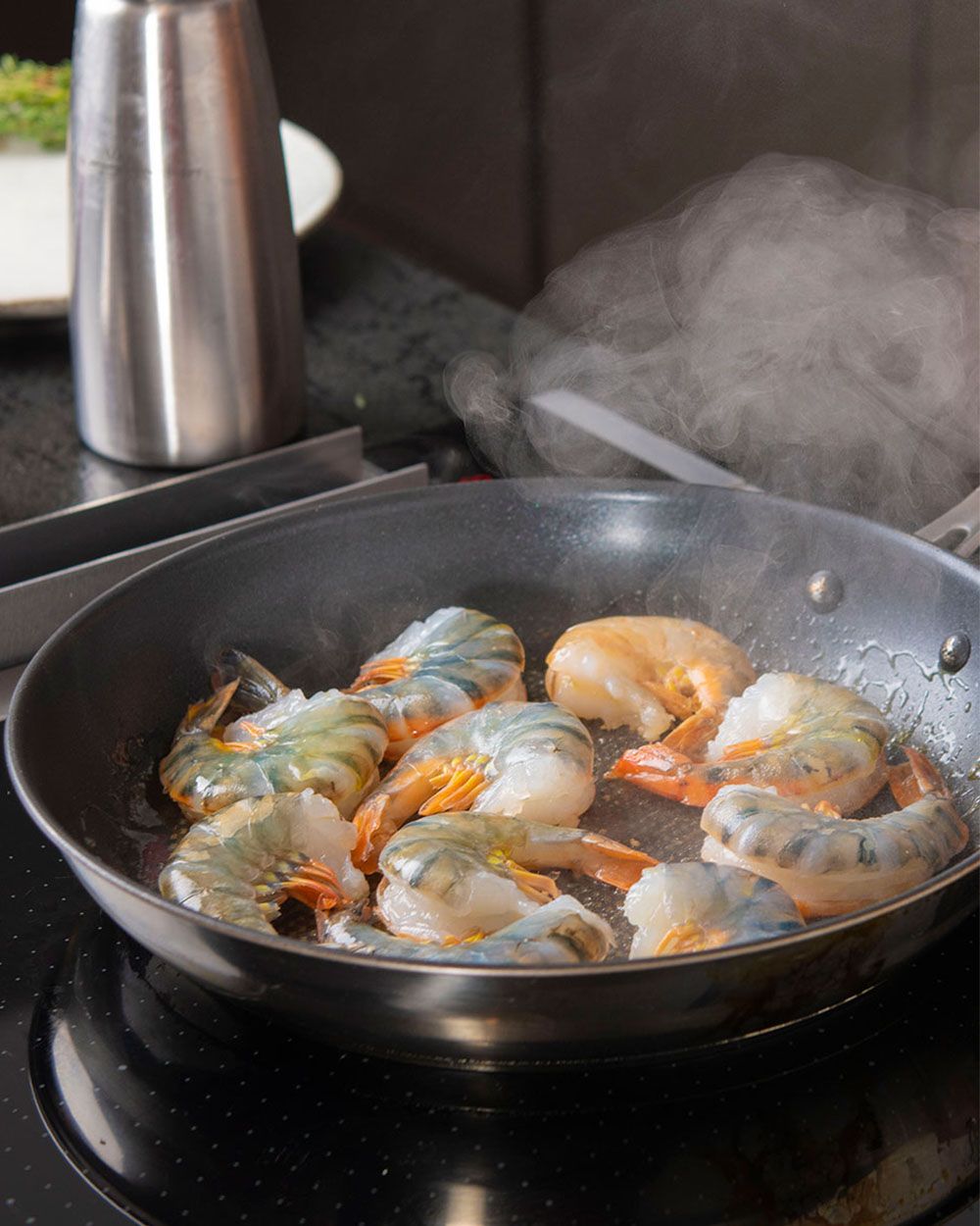 In einer Pfanne werden Shrimps angebraten, im Hintergrund steht eine iSi Gourmet Whip. 