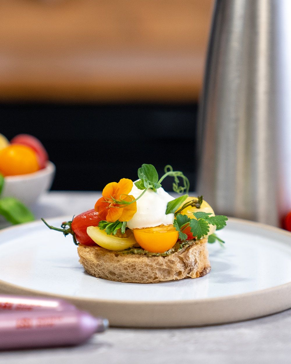 Ein Teller mit einem Tomaten-Tarte mit Burrata, davor iSi Charge Kapseln. 