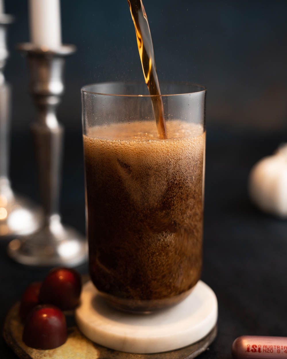 Jemand gießt Kaffee in ein Glas, im Hintergrund ein Kerzenständer.