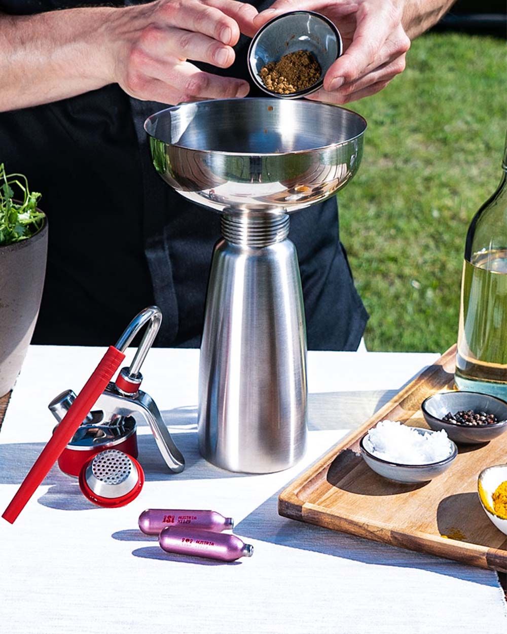 Jemand gibt Gewürze in ein iSi Gourmet Whip, daneben weitere Gewürze und iSi Charge Kapseln. 