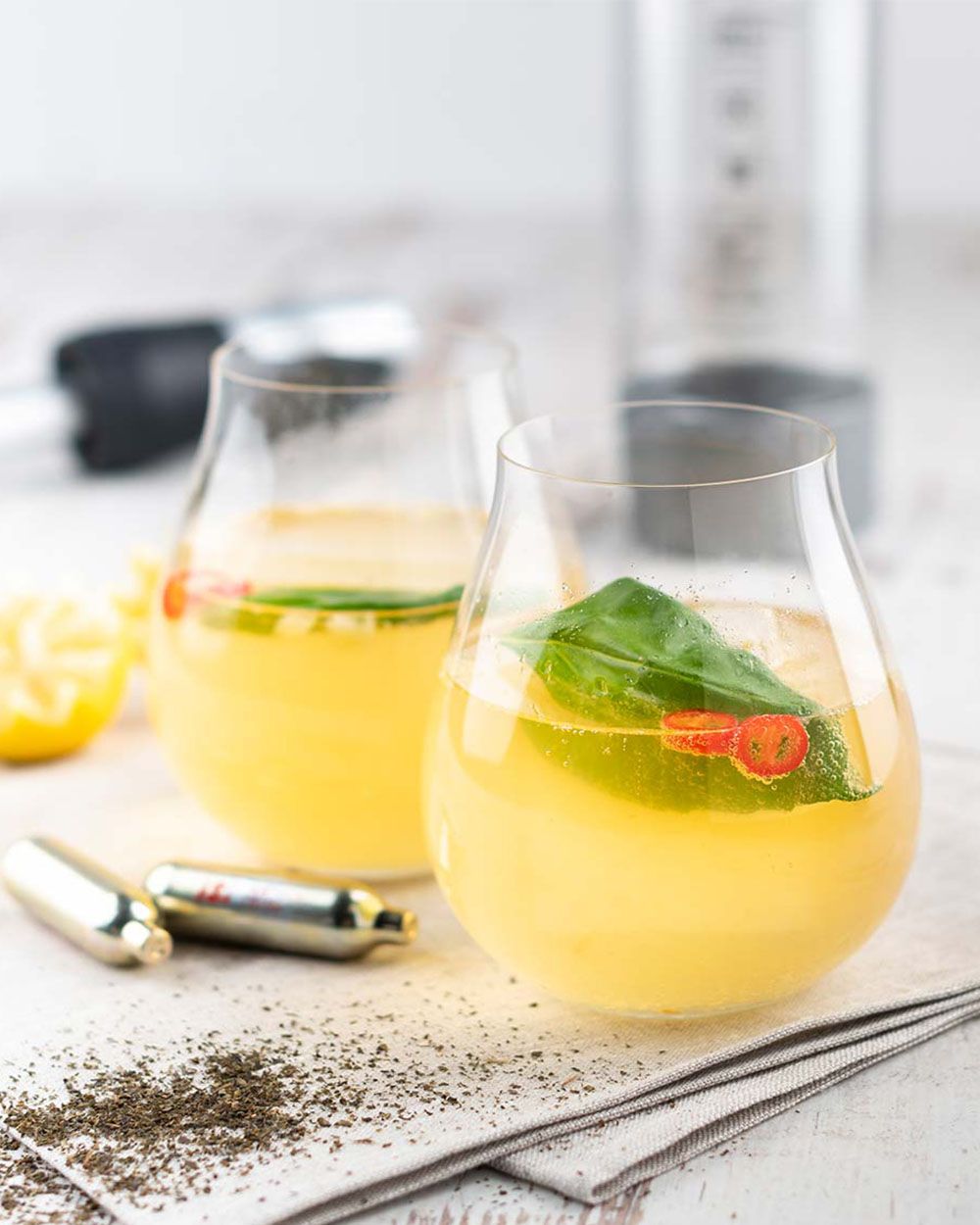 Zwei Gläser mit einem Eistee-Getränk, daneben iSi Charge Kapseln. 