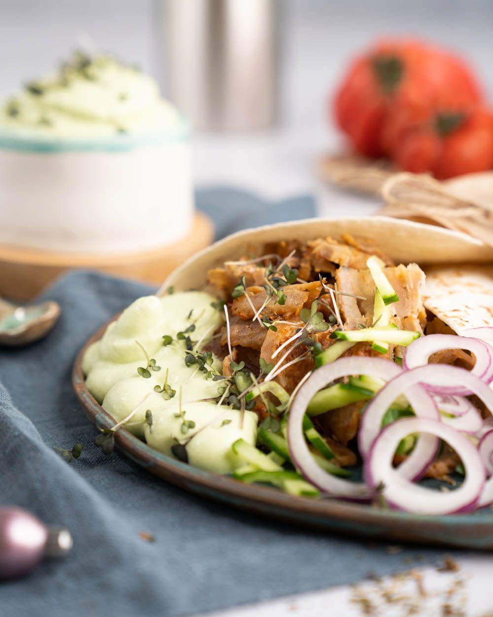 Ein Teller mit Gyros, im Hintergrund eine Schüssel mit Tzatziki Espuma und Tomaten. 