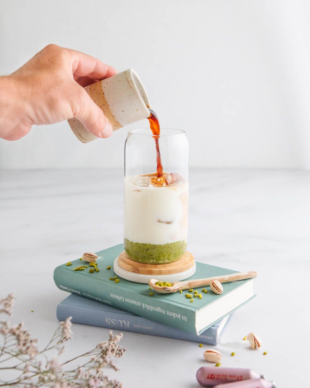 Jemand gießt Kaffee in ein Glas mit Milch und Pistazie. 