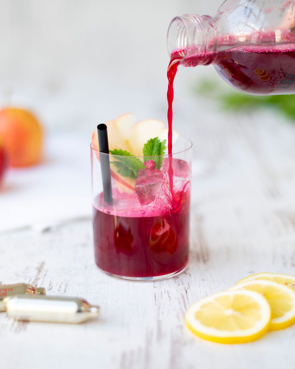 Jemand gießt ein dunkelrotes Getränk, genannt Red Detox, in ein Glas, daneben Zitronenscheiben und iSi Charge Kapseln. 