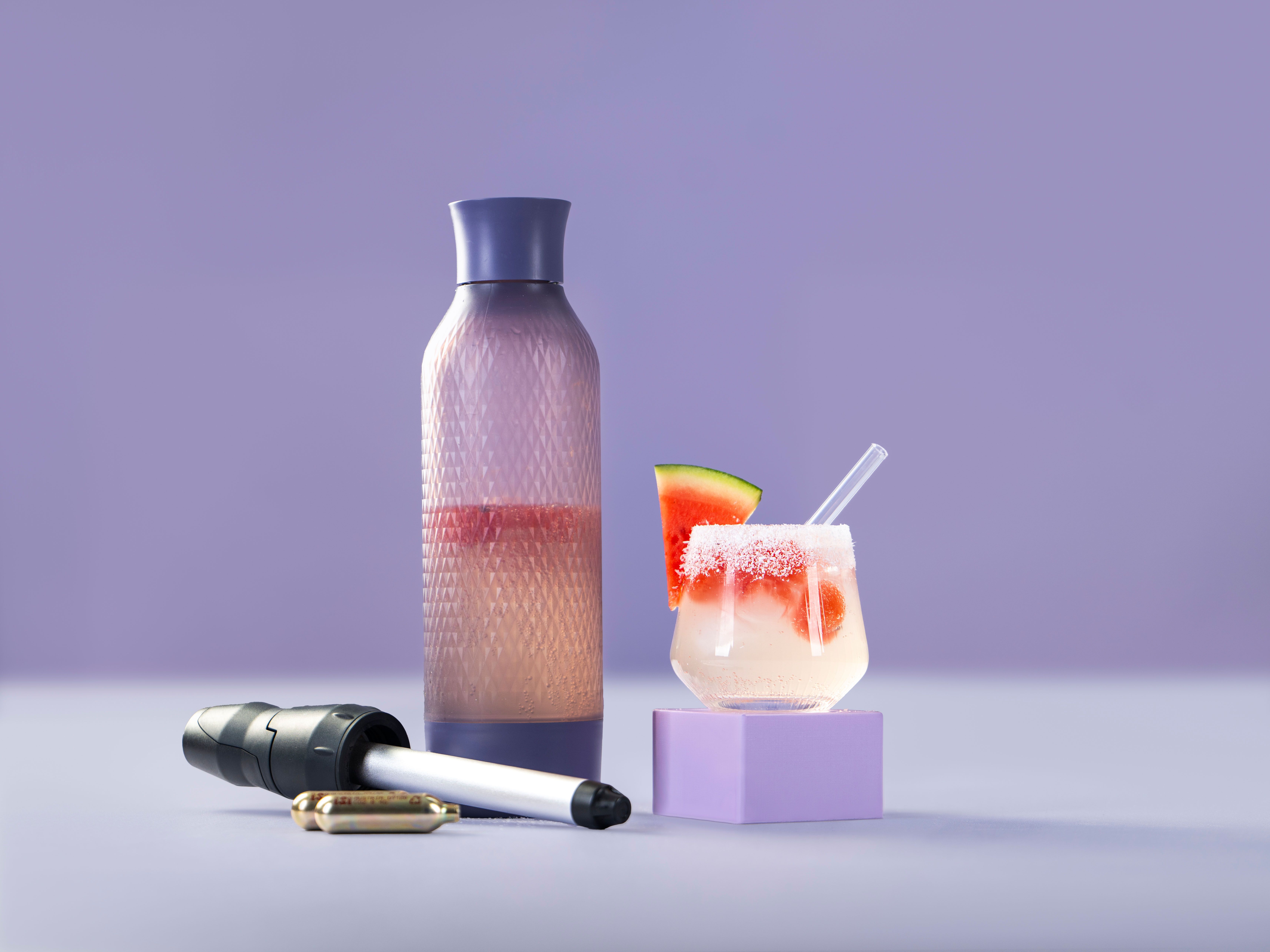 Ein Glas mit einem Getränk, Sparkling Cocomelon, daneben ein iSi Twist'n Sparkle und iSi Charge Kapseln.