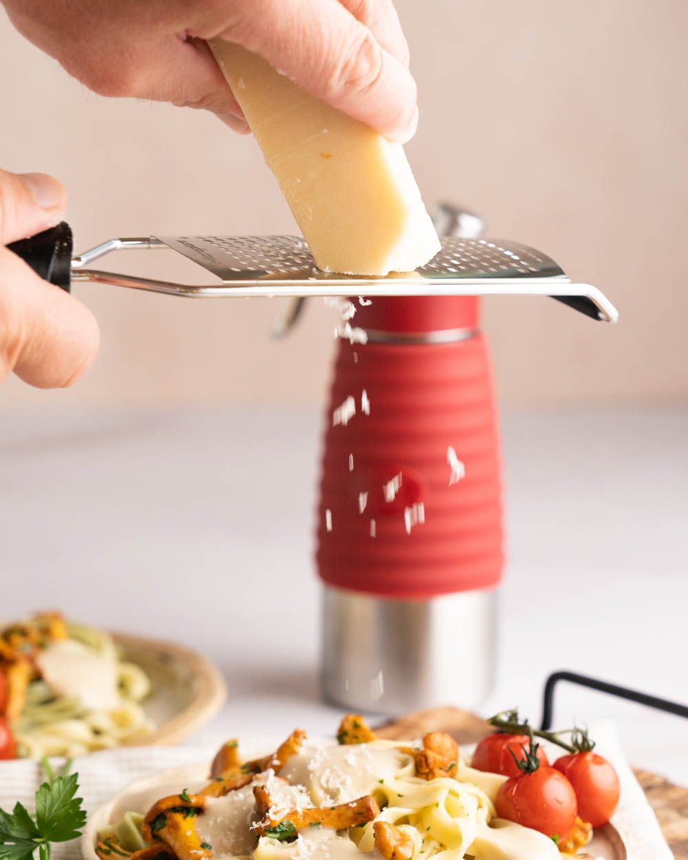 Jemand reibt Parmesan über einem Teller Pasta mit Pilzrahmsauce. Im Hintergrund steht ein iSi Gourmet Whip. 