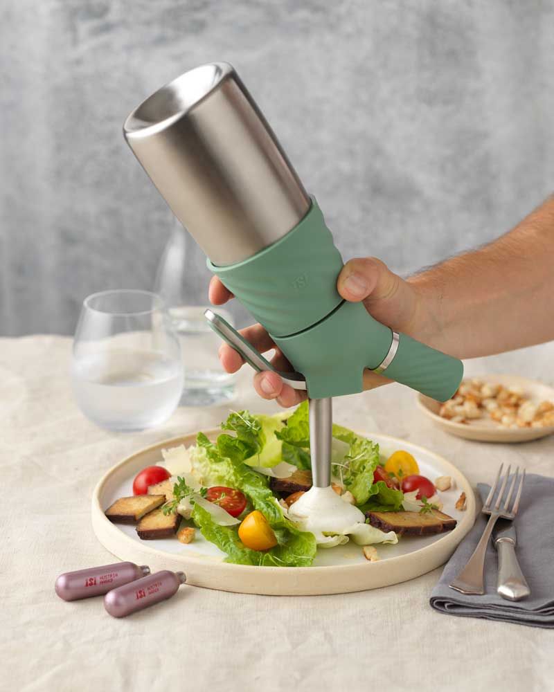 Auf dem Bild wird mit einem iSi Creative Whip eine Creme als Dressing über einen frischen Salat mit Tomaten, Croûtons und Parmesan gegeben.