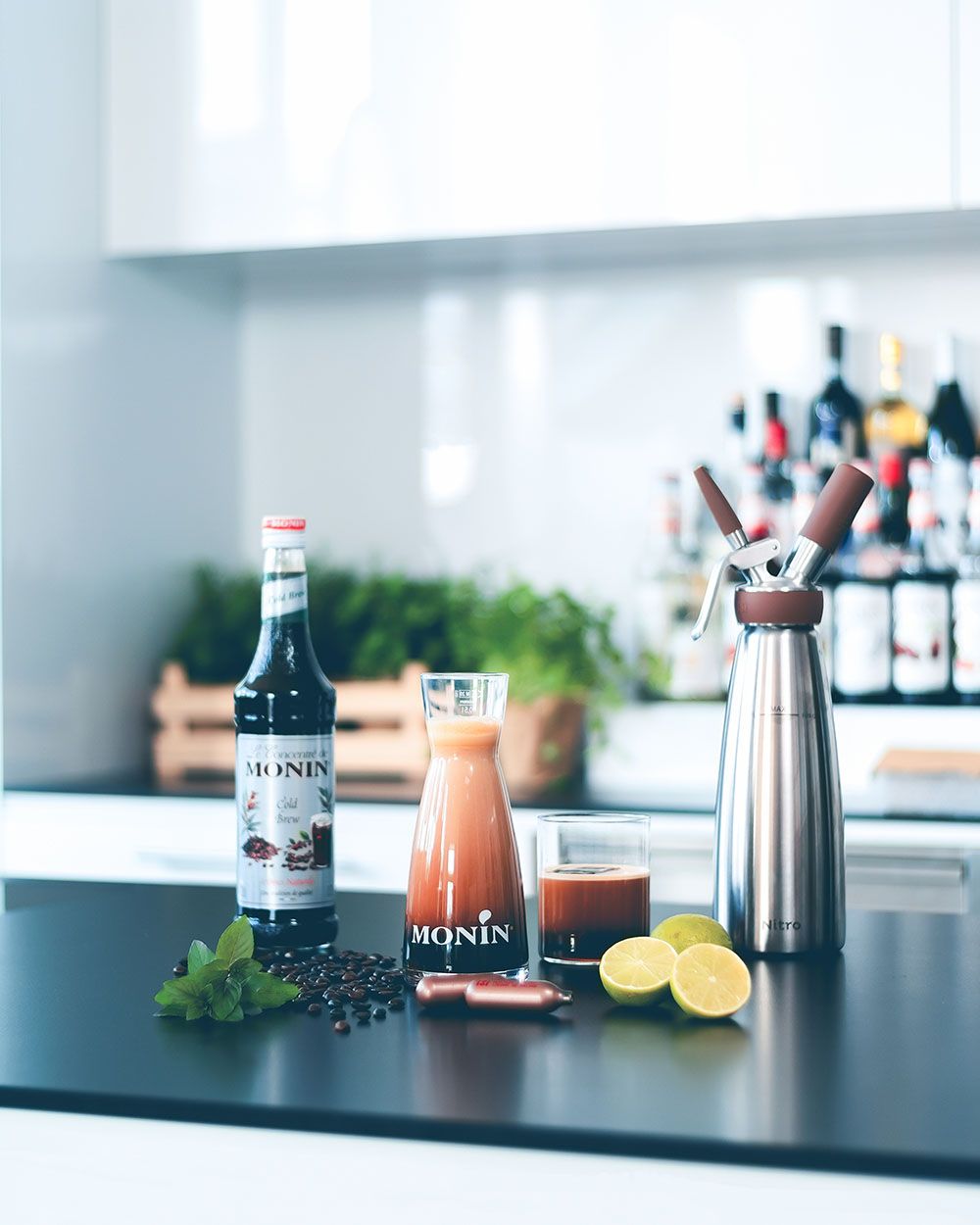 Ein Hibiskus Kombucha Getränk, daneben ein Monin Sirup, zwei iSi Charge Kapseln, Limetten und ein iSi Nitro.