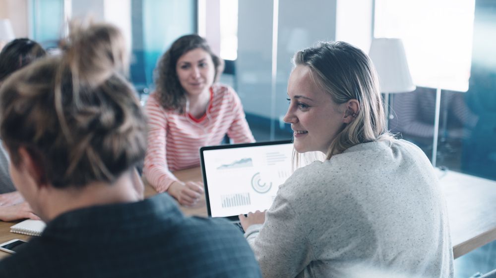 Mehrere Frauen sitzen gemeinsam an einem Tisch  und arbeiten mit Laptops gemeinsam an einem Projekt. 