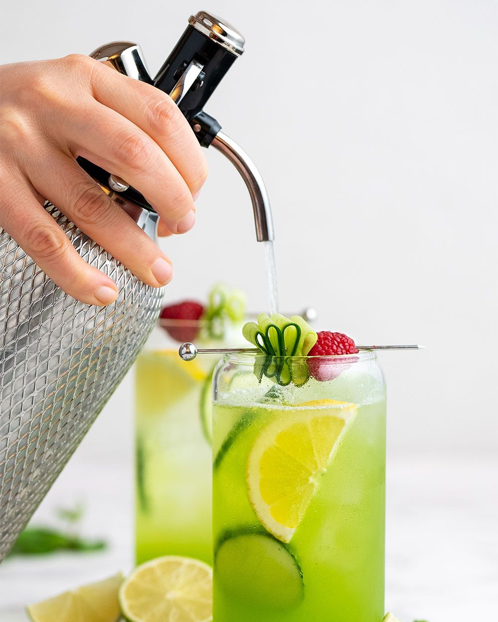 Jemand gibt Soda aus einem iSi Soda Maker in ein Glas mit Nitro Gurken Gin. 