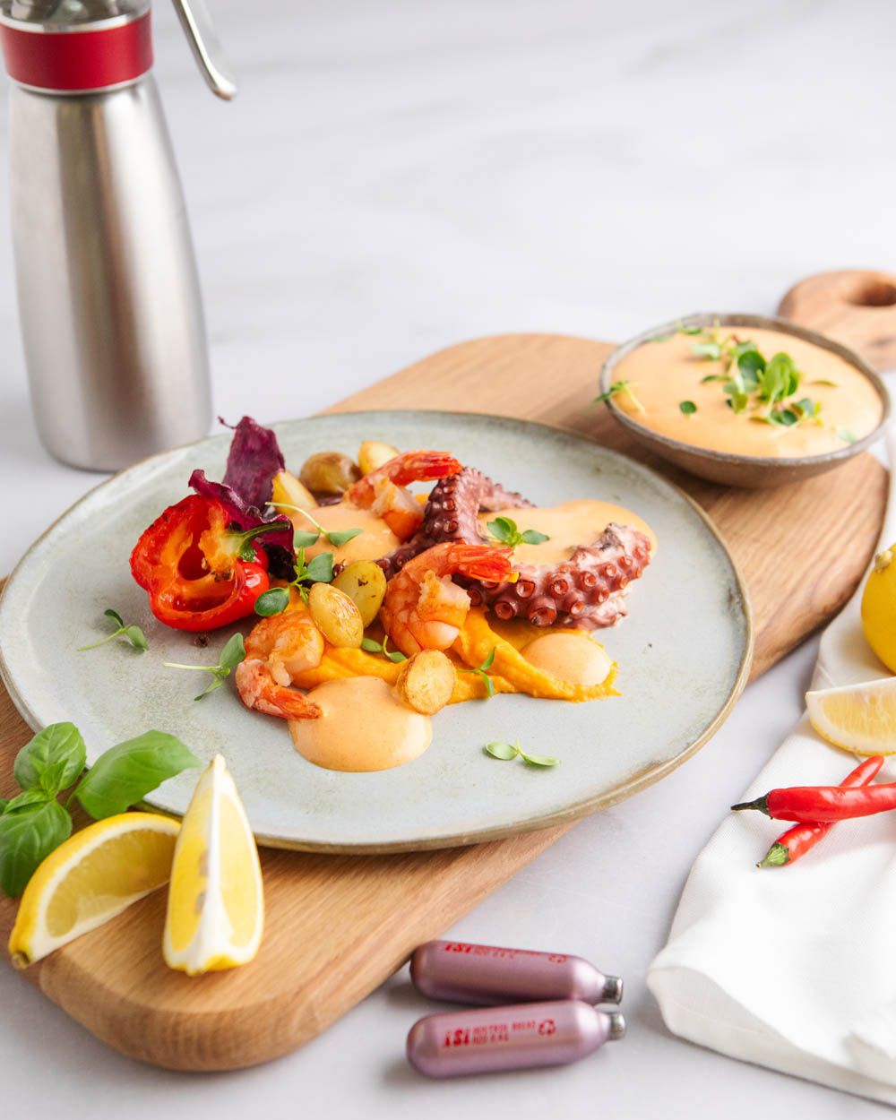 Ein Teller mit Meeresfrüchten und Chilli Mayonnaise. Daneben eine Schüssel mit mehr Sauce, Zitronen und zwei iSi Charge Kapseln.