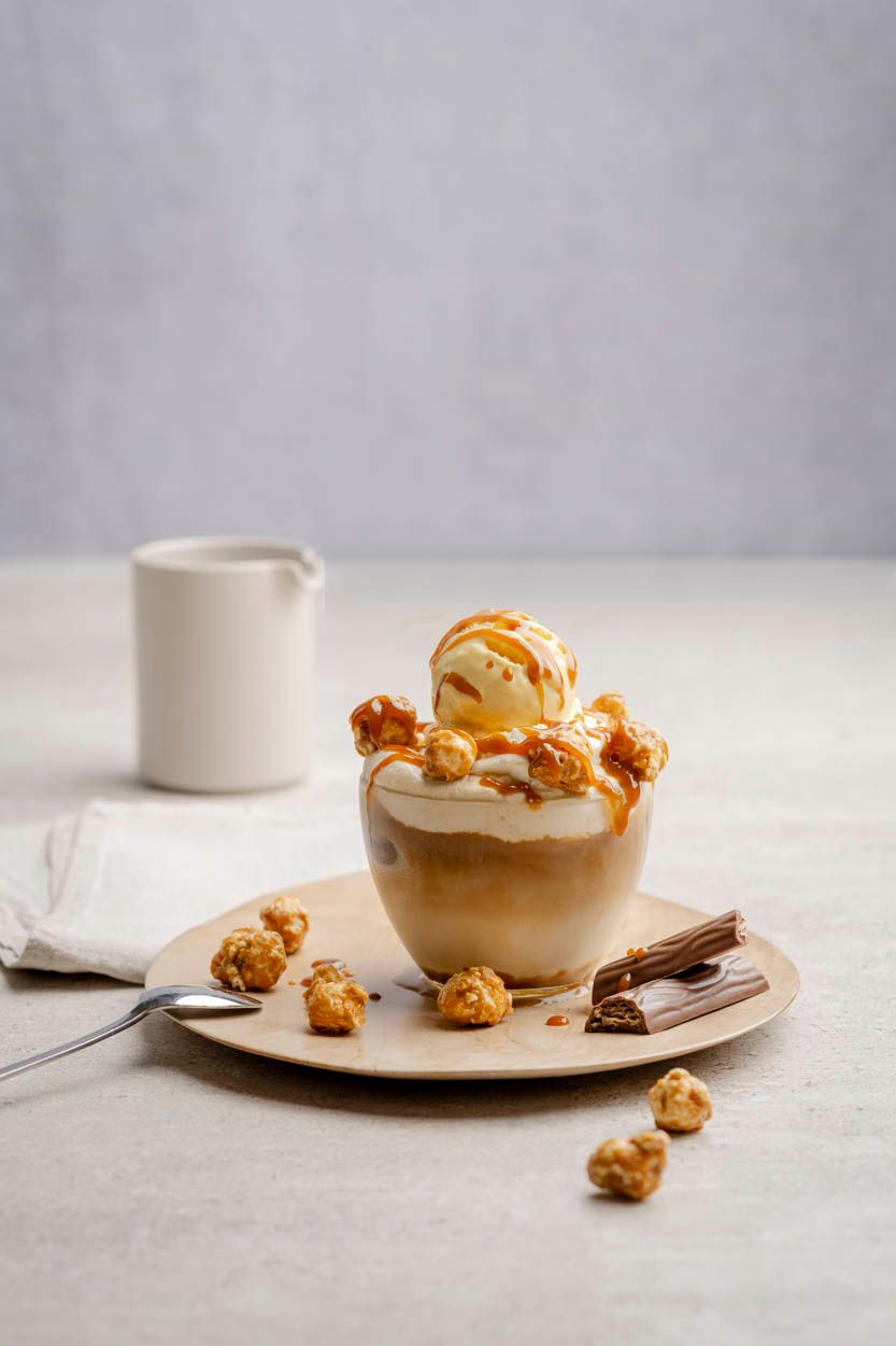 Auf einem Teller liegen Haselnüsse und Schokoriegel und ein Glas mit einem Affogato Kaffee. 