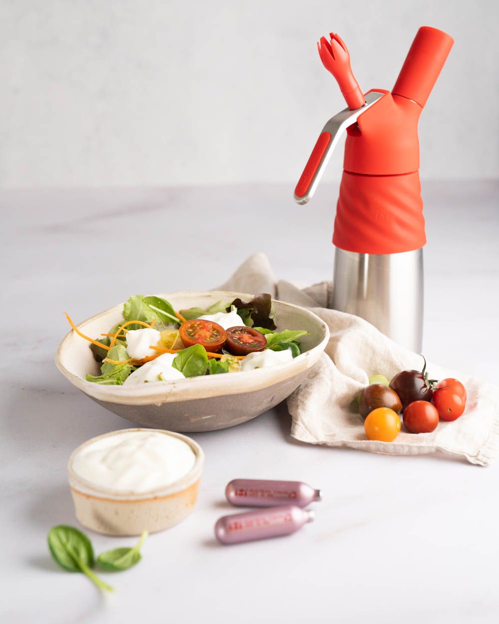 Eine Schüssel mit Sour Cream Dressing und eine Schüssel mit Salat, daneben iSi Charge Kapseln, Tomaten und ein iSi Creative Whip.